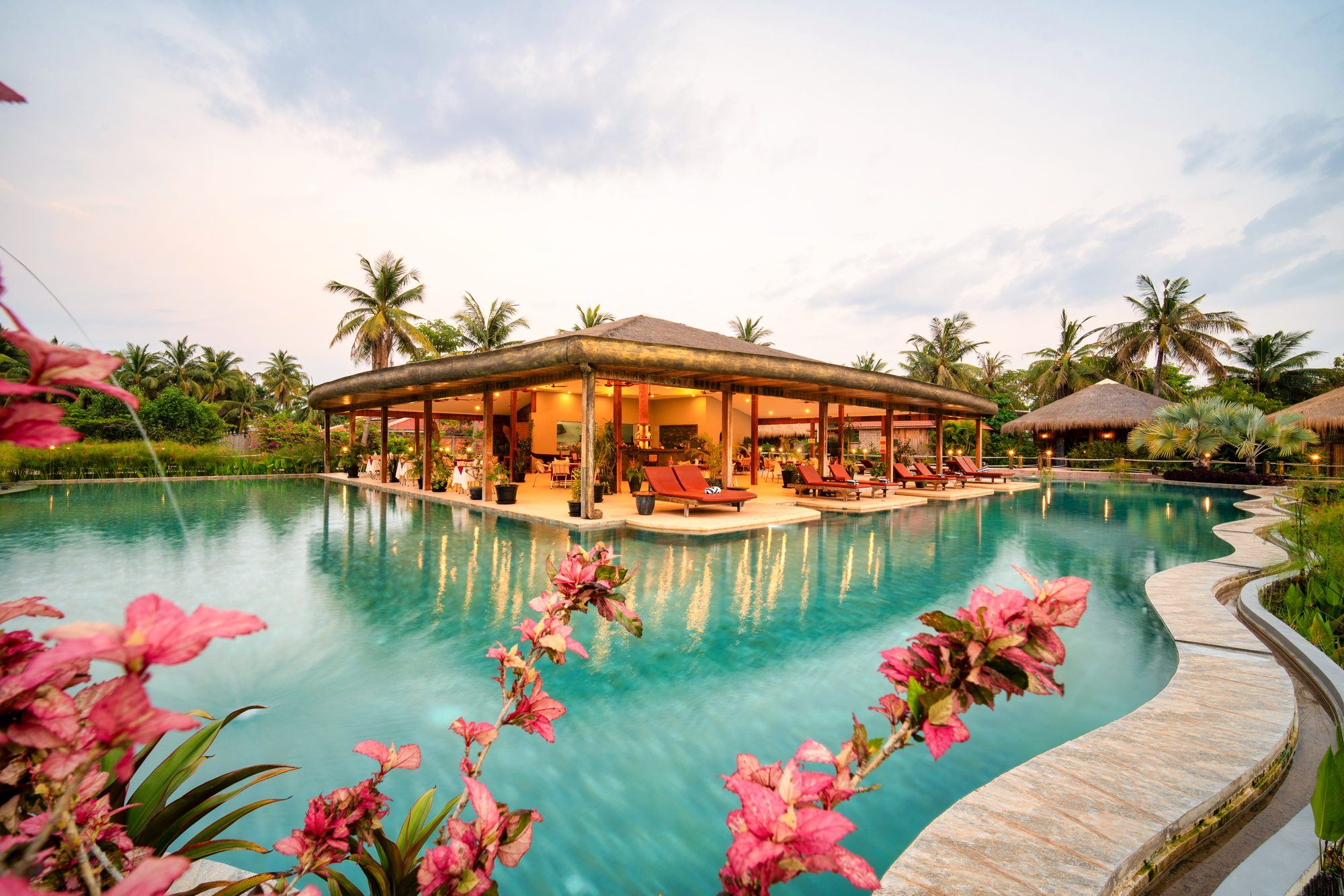 La grande piscine et le pavillon du restaurant au milieu de l'eau, des fleurs roses au premier plan
