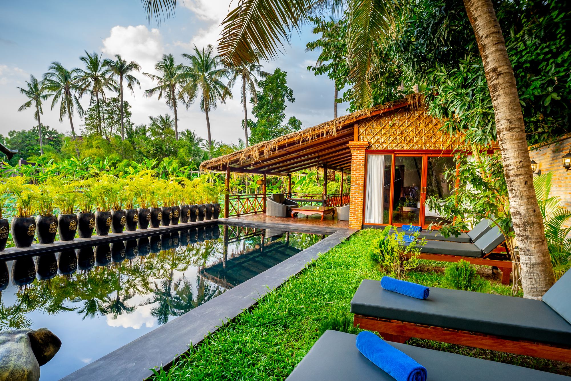 Villa Coconut's private pool lined with Khmer jars, its thatched terrace and sun loungers under the palms