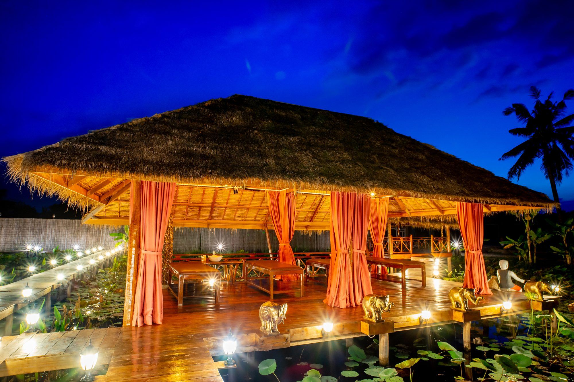 Thatched spa pavilion over the lotus lake, lit at blue hour